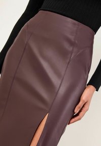 Fustă creion din piele eco bordeaux, cu o deschidere laterală, având cusături decorative și un finisaj neted. Designul aderent evidențiază silueta.