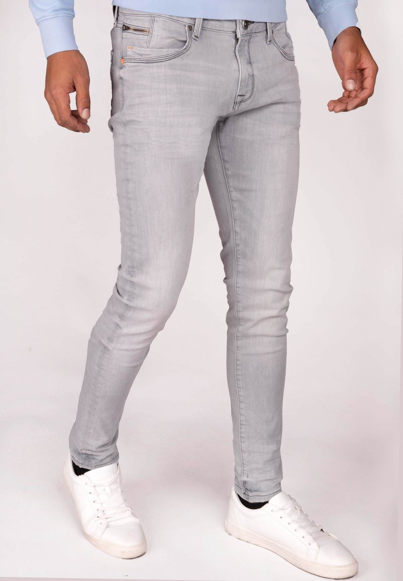 Jeans aderenti grigio chiaro in denim, con cinque tasche, cerniera e lievi sfumature. Abbinati a sneakers bianche.