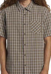 Chemise à manches courtes à motif carreaux marron et blanc, avec des boutons, un col, et une poche poitrine avec des rayures diagonales.