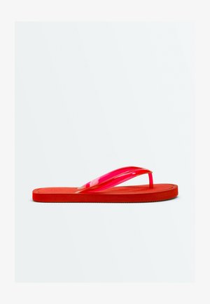 Une sandale tong rouge unique avec une semelle plate et des brides rouges translucides brillantes sur un fond blanc uni.