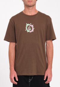 Camiseta de algodón marrón con mangas cortas y cuello redondo. Presenta un diseño gráfico multicolor con estrellas y un logotipo en el pecho.