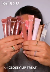 Åtte rør med IsaDora Glossy Lip Treat i forskjellige nyanser av rosa, brunt og klart, med glossy finish og etiketter på forsiden.