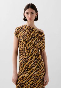 Asymmetrisk kjole i gul og brun med et leopardmønster. Blødt, draperet stof med design med én skulder og korte ærmer.