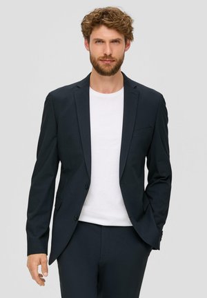 Blazer bleu marine à coupe ajustée, avec deux boutons sur le devant et un col à revers. Porté sur un t-shirt blanc, il présente des poches latérales et une texture lisse.