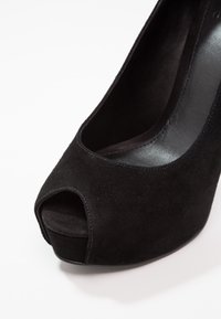 Chaussure à talon haut en daim noir avec ouverture sur les orteils et semelle compensée, vue en gros plan sous un angle.