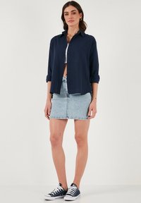 Camicia blu navy con bottoni e maniche lunghe, gonna di jeans light blue, e sneakers blu navy. Design semplice con una vestibilità casual e rilassata.