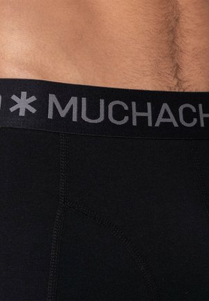 Fekete boxernadrág szürke derékrésszel, amelyen a "MUCHACHO" felirat található. Az anyag sima, és a varrások jól láthatók az illeszkedéseknél.
