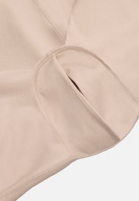 Tela de color beige claro con una textura suave, que presenta un detalle de bolsillo curvado y costuras visibles alrededor de los bordes.