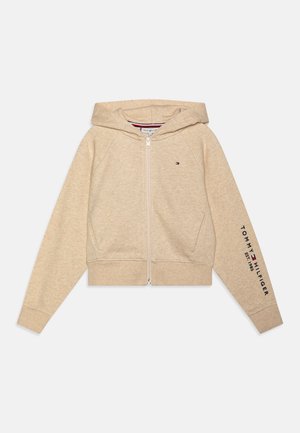 Beige Kapuzenjacke mit Reißverschluss, vorderen Taschen, Kapuze und dem Schriftzug sowie Logo "Tommy Hilfiger Est. 1985" auf dem linken Ärmel.