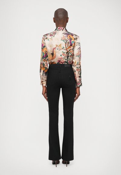 Camisa de manga larga con estampado floral en colores vivos, combinada con jeans negros ajustados y zapatos de tacón, vista desde la parte de atrás.