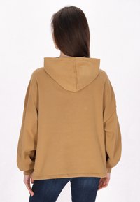 Braune übergroße Kapuzenjacke mit einer großen Kapuze auf der Rückseite, überschnittenen Schultern und weichem Stoff. Sichtbare Nähte und entspannter Schnitt.
