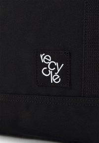 Black fabric bag featuring a textured surface and a label with the word "recycle" in white, prominently displayed.
