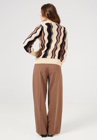 Jersey de punto colorido y ondulado con base color crema y acentos en púrpura, marrón y azul; puños y dobladillo acanalados; combinado con pantalones de pierna ancha marrones.