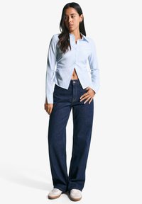 Gestreept lichtblauw overhemd met knopen en lange mouwen, met een getailleerde taille, gecombineerd met donkerblauwe wijde jeans en lichte sneakers.