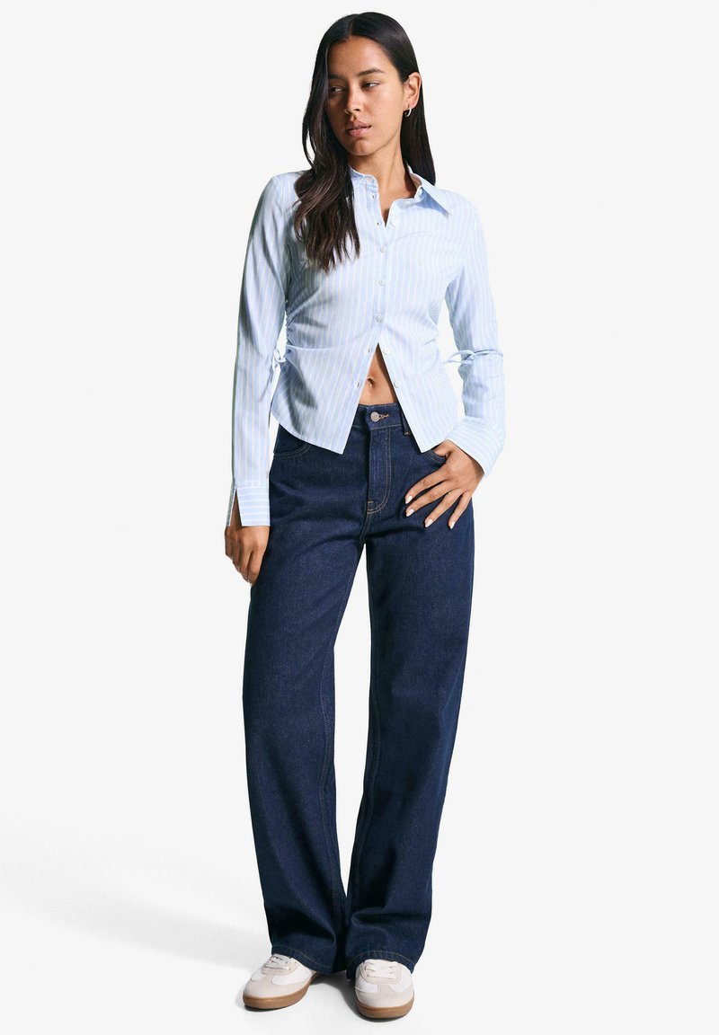 Gestreept lichtblauw overhemd met knopen en lange mouwen, met een getailleerde taille, gecombineerd met donkerblauwe wijde jeans en lichte sneakers.