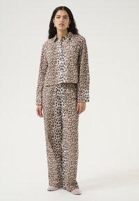Twee-delige set met luipaardprint, bestaande uit een geknoopte shirt met kraag en een wijde broek, gemaakt van soepele stof met een glanzende afwerking.
