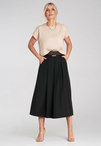 Beige Kurzarmoberteil, kombiniert mit einem schwarzen, plissierten Midirock. Das Outfit verfügt über einen breiten braunen Gürtel mit einer silbernen Schnalle und Taschen im Rock.