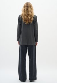 Grå skræddersyet blazer med lange ærmer, parret med brede sorte denimbukser. Glat stof med en subtil tekstur.