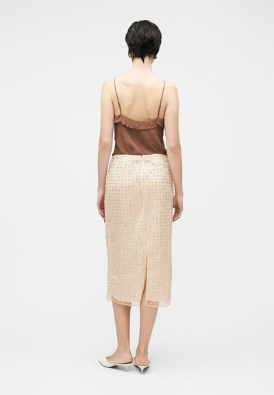 Camisole en satin marron à fines bretelles associée à une jupe crème mi-longue avec un motif texturé et une fente à l'arrière.