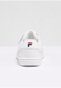 Vit sneaker med en slät läderövre, vadderad häl och textil tunga. Har röda och blå logotypdetaljer på hälen. Platt gummisula.