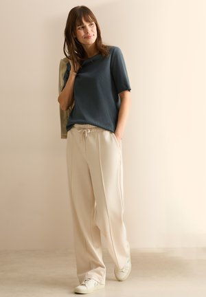 Haut bleu à manches courtes, pantalon crème avec cordon de serrage, et baskets blanches. Textures lisses avec une coupe décontractée et poches latérales sur le pantalon.