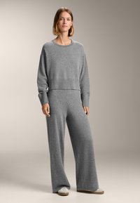Grau geschnittener Pullover mit ribbeligem Saum, kombiniert mit grauen, weit geschnittenen Hosen. Weiche Textur, lässige Passform und neutrales Farbschema.