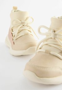 Sneakers alto beige chiaro con tomaia sintetica liscia, punta rotonda e accentuazione decorativa rosa sul lato, dotati di suole in gomma testurizzata.