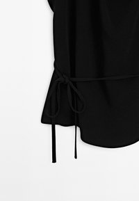 Top nero realizzato in tessuto morbido, dotato di cintura annodata con lunghe e sottili tracolle e orlo curvo. Design semplice senza motivi.