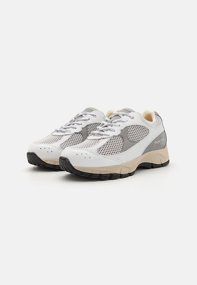 Baskets de sport blanches et grises avec une tige en maille, bout rond, col rembourré et semelle en caoutchouc noir texturé avec des accents beiges.