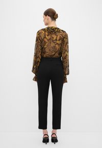 Doorzichtig, gemusterd blouse met ruches aan de hals in herfstkleuren, gecombineerd met stijlvolle zwarte broek en zwarte hakken met bandjes.