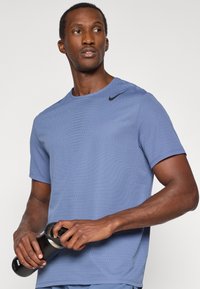 T-shirt atletico Nike di colore azzurro chiaro con maniche corte, tessuto testurizzato con perforazioni e logo Swoosh Nike nero sulla spalla.