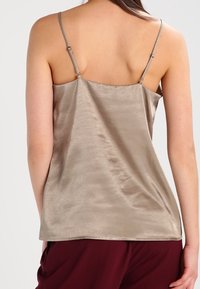Satinová košilka v jemné béžové barvě s nastavovacími ramínky a hladkou texturou, s jednoduchým, elegantním designem.