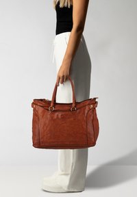 Borsa tote in pelle marrone con due manici e rifiniture in tonalità dorata, caratterizzata da una superficie texturizzata e chiusura a zip, esposta su uno sfondo neutro.