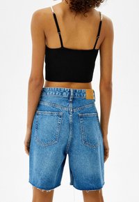 Svart ribbad crop top med tunna justerbara axelband, kombinerad med högmidjade blå denim shorts med fransade kanter och två bakfickor.