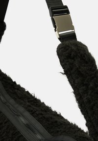 Sac à épaule noir en fourrure doté d'un tissu doux et texturé, d'accents en cuir noir lisse et d'une bandoulière robuste et réglable avec une boucle métallique.