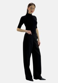 Figursyet sort rullekrave-top kombineret med højtaljede, sorte bukser med vide ben. Glat stof, minimalistisk design og slank silhuet.