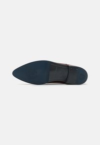 Suola di scarpa in pelle marrone con punta affusolata, dotata di un fondo in gomma nera e blu scuro testurizzato. Dettaglio del logo in rilievo vicino al tallone.