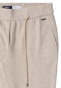 Béžové kalhoty s vzorem herringbone, elastickým pasem, šňůrkou a kovovým akcentem poblíž kapsy. Měkká textura.