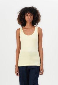 Top de tirantes ajustado amarillo claro con tirantes anchos y escote redondeado. Textura suave y diseño sin costuras. Combinado con pantalones azul oscuro.