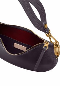 Bolso de cuero morado oscuro con una cremallera dorada, que presenta un interior rojo profundo y una correa texturizada gris. Incluye un acento de herrajes dorados.
