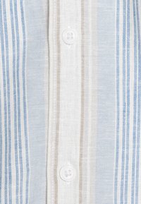 Lichtgewicht gestreepte stof in blauw- en beige tinten, met een knoopsluiting en een gestructureerde linnenachtige weving.