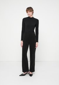 Fekete, testhez álló, hosszú ujjú felső, amely finom csillogással rendelkezik, magas derekú fekete, bőszárú nadrággal és hegyes orrú fekete magas sarkú cipővel párosítva. Az anyag sima textúrájú.