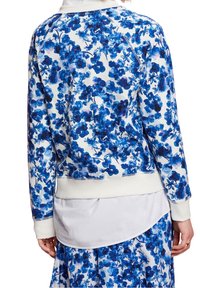 Blommig sweatshirt med ett blått blommönster på vit bakgrund, ribbade muddar och en avslappnad passform, lager på ett vitt plagg.