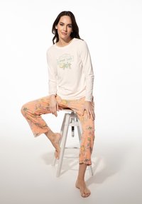 Crème lange mouwen top met "Lemon Lover" print, gecombineerd met pastel oranje broek met citroen- en bloemenpatronen, terwijl zittend gedragen.