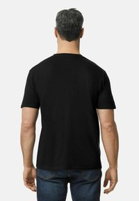 Camiseta de algodón negra con mangas cortas, escote redondo y corte recto, llevada por una persona vista desde atrás.