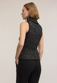 Svart ärmlös topp med hög hals, texturerat stickat tyg med silverglitter, figurnära siluett och lätt peplum i midjan.