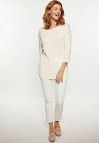 Pulover crem din tricot cu un model în zigzag, decolteu larg și mâneci trei sferturi, asociat cu pantaloni skinny albi și mocasini bej deschis.