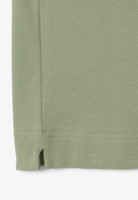 Tessuto testurizzato in un morbido colore verde con un leggero orlo e una fessura laterale, che mette in mostra un design traspirante e casual adatto per il clima caldo.
