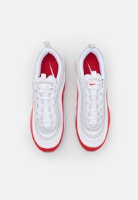 Scarpe sportive bianche con dettagli rossi, caratterizzate da una superficie testurizzata, design stratificato e chiusura con lacci. Logo Nike ben visibile sulla linguetta.