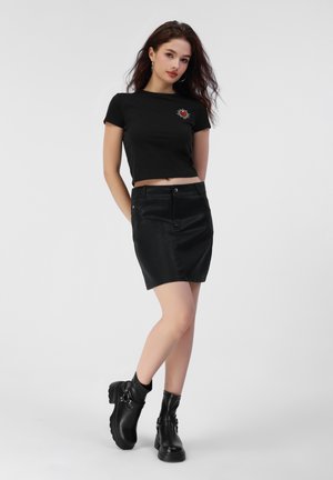 Black cropped t-shirt with a red heart graphic, paired with a black leather mini skirt and chunky black ankle boots.